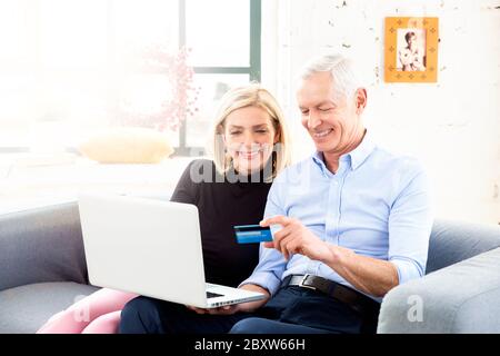 Shot of happy senior couple shopping online. Attractive elderly woman and senior man man sitting on couch behind their laptop and making online paymen Stock Photo