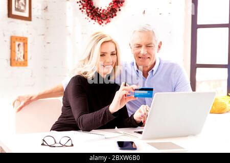 Shot of happy senior couple shopping online. Attractive elderly woman holding bank card in her hand while senior man sitting behind their laptop and m Stock Photo