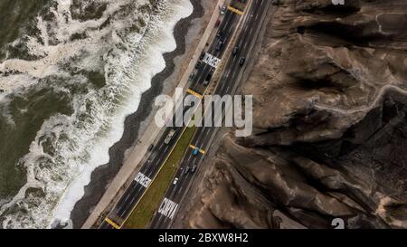 Aerial photo of the highway next to the Pacific Ocean in Lima, Peru, in between crashing waves and brown cliffs. Stock Photo