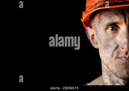 The face of a male miner in a helmet on a black background. Stock Photo