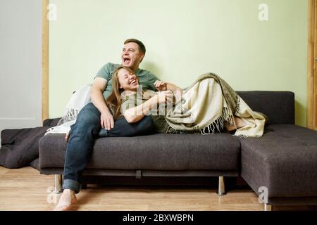 Young couple in casual clothes embracing on couch, talking and laughing, stay home concept, full body Stock Photo