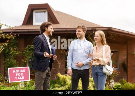 Young family talking to real estate agent about purchasing property near beautiful house outside Stock Photo