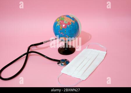 Medical mask, stethoscope and earth globe on pastel background. Stock Photo