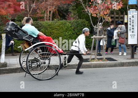 A young rickshaw driver is pulling two tourists in Arashiyama, Kyoto, Japan Stock Photo