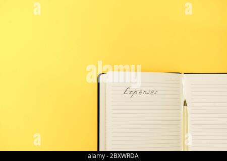 Expenses and budget planning concept. Top view of notepad with handwritten words Expenses on yellow background with copy space Stock Photo