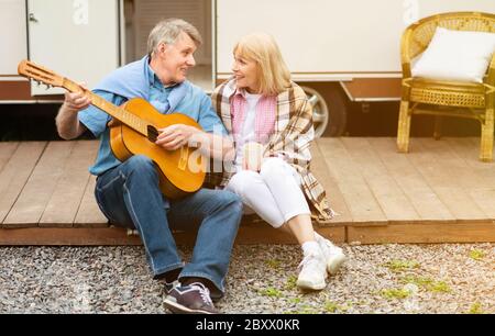 Handsome senior man with guitar performing song to his sweet wife near their recreation vehicle outdoors Stock Photo