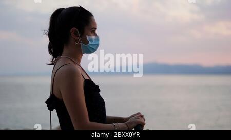 side woman wearing mask looking at infinity against sunset background Stock Photo