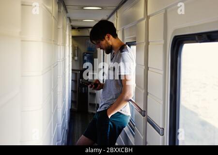 Handsome young caucasian man with a beard, looking at a smartphone in the hallway by the window . Travel leisure Stock Photo
