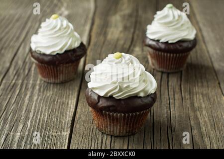 Homemade chocolate cupcakes in cupcake liners, topped with whipped cream, decorated with button-shaped candies, on the rustic wood plank background. Stock Photo