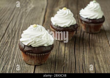 Chocolate cupcakes in paper patty cases, topped with whipped cream and decorated with button-shaped candies, on the rustic wood planks. Stock Photo