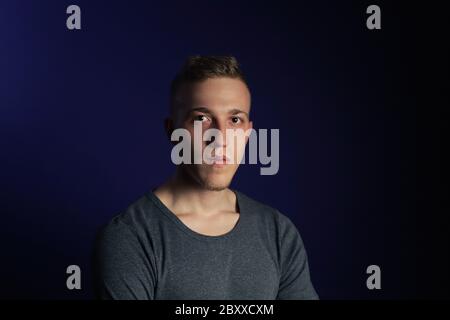 Young caucasian blonde man in grey t shirt on dark purple background Stock Photo