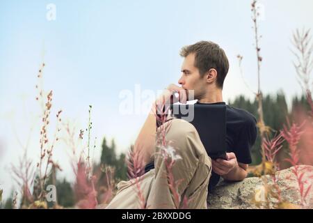 Handsome young concentrated man freelancer working on a laptop outdoors in mountains. Freelance concept Stock Photo