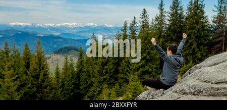 A man is high in the mountains against the sky, celebrating the victory, raising his hands up. Stock Photo