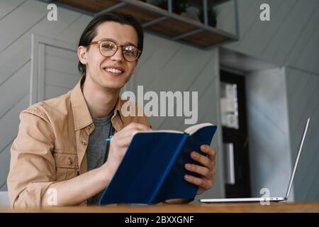 Student studying, distance learning. Smiling hipster man taking notes in notebook, working freelance project from home Stock Photo