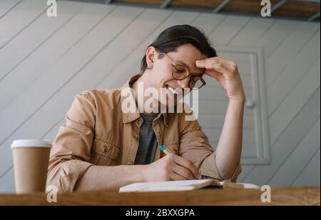 Handsome man working freelance project, planning strategy at workplace. Happy student studying, taking notes in notebook, reading. Education concept Stock Photo
