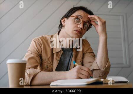 Busy, tired man looking for creative solution, thinking, brainstorming at workplace. Pensive hipster in stylish eyeglasses working freelance project Stock Photo