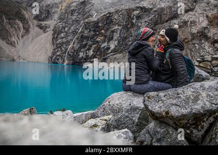 romantic couple sitting on a rocks near a turquoise lake in the middle of mountains