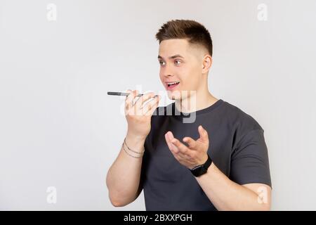 A young man, a guy talking to a friend on the phone, recording a voice message or a note in a smartphone application, holding a mobile phone near his lips close to the speaker, talking to an assistant Stock Photo