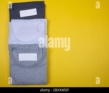 Dark Grey, Grey and White T-Shirts on Bright Yellow Background. Stock Photo