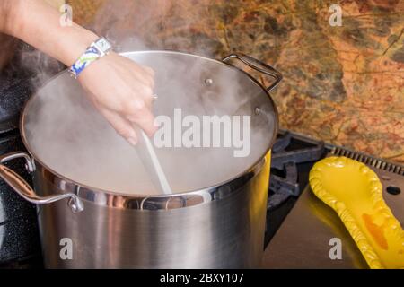 Woman stirring a boiling pot of apricot jam, with heavy steam Stock Photo