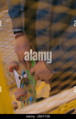 Portrait shot of man holding skateboard through a yellow metal grate Stock Photo