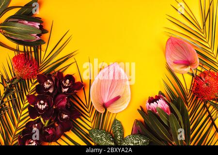 Orchid, anthurium, protea and palm leaves on yellow background. Tropical flowers flat lay pattern with place for text. Stock Photo