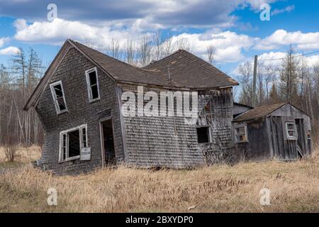 An abandoned house that is collapsing in a field. Windows and door broken out, no trespassing sign on front. Blue sky with clouds. Stock Photo