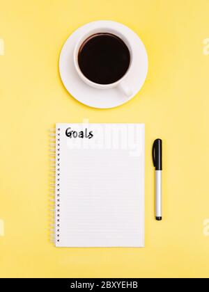 Goals Top view photo Inspirational poster with notebook and cup of black coffee on yellow background Stock Photo