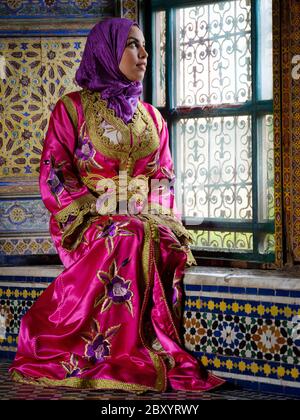 FEZ, MOROCCO - CIRCA MAY 2018:  Young Moroccan woman in traditional dress seating by a window in Fez Stock Photo