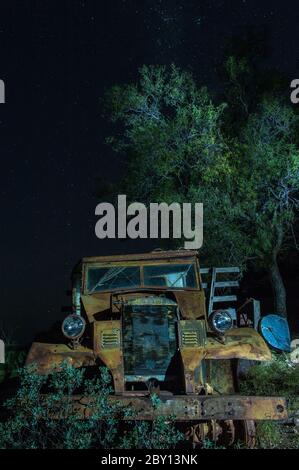 Old abandoned farm truck lays rusting on a western Queensland property, machinery graveyard blanketed by the clear night sky and a lone tree. Stock Photo