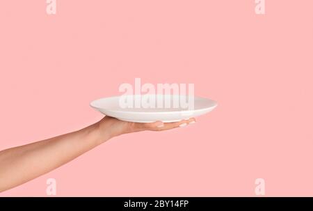 Millennial woman holding empty plate on pink background, mockup for design Stock Photo