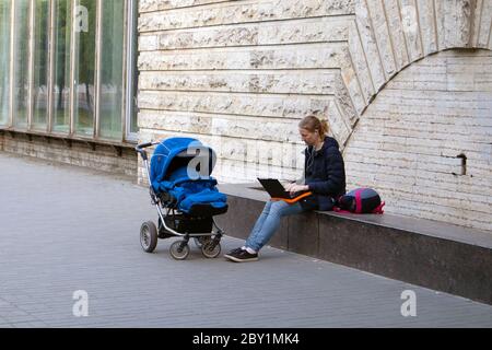 Young woman with baby carriage near working on laptop outdoors Stock Photo