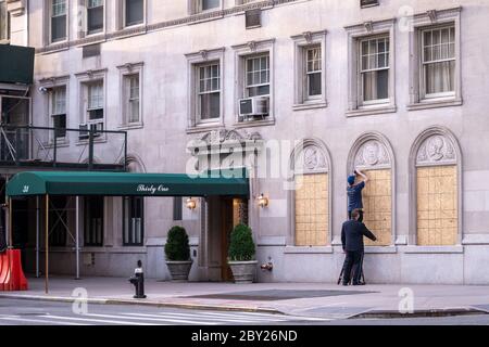 New York, USA. 8th June, 2020. A doorman of an upscale building in New York City's Upper East Side helps a repairman secure plywood protections. Many stores and buildings covered their windows in case of rioting even as the city entered the first phase of reopening after the coronavirus lockdown. Credit: Enrique Shore/Alamy Live News Stock Photo