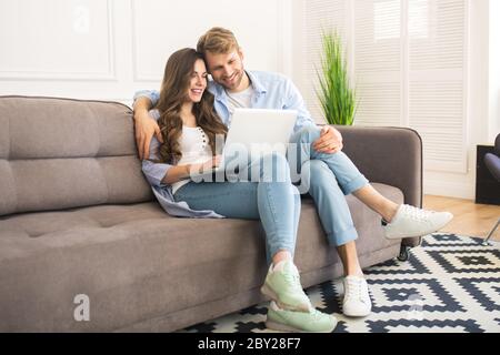 Young couple in denim sitting on a sofa and watching a movie Stock Photo