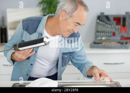 senior man using caulk gun around a sink Stock Photo