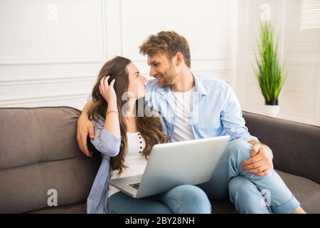 Young couple in denim sitting on a sofa looking at each other and feeling happy Stock Photo