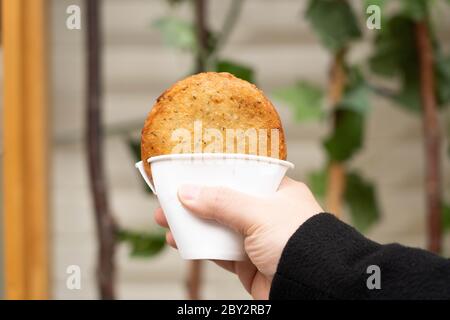 Hand holding a Korean traditional street food, deep fried pancake, Hotteok, with sweet fillings in a cup. Stock Photo