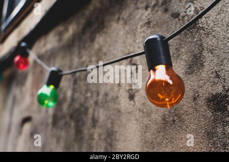 Colorful light bulbs decoration hanging on a wall in an alley. Stock Photo