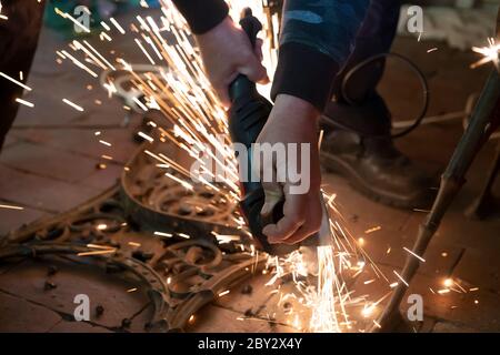 Front view of a man's hands working on a metal part of a garden bench, using an electric grinder while sparks are flying around in the industrial Stock Photo
