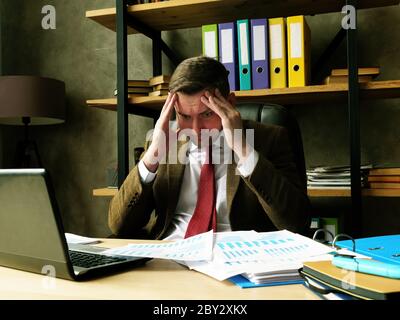 A frustrated, tired businessman reads a statement of financial loss. Stock Photo