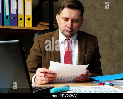 A man in a suit works with papers and checks data with graphs. Office work routine. Stock Photo