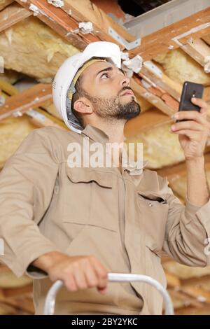 builder stood on stepladder holding smartphone Stock Photo