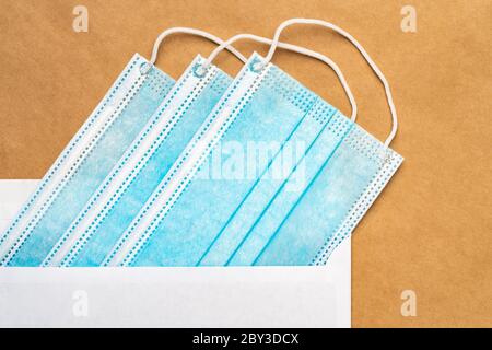 Blue medical surgical face mask in white postal envelope on yellow craft paper background. Flat lay, close-up view. Concept caring for loved people Stock Photo