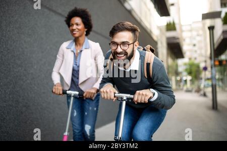 Two smiling business people driving electric scooter going to work. Stock Photo