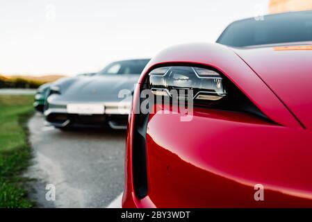 Alesund / Norway - May 31, 2020: Three luxury Porsche Taycan sedans in a parking lot, parked for promotional purposes. Headlight close up shot. Stock Photo