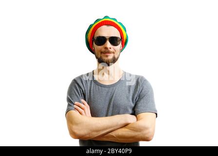 Young caucasian smiling man in rasta hat, sunglasses and grey t-shirt on white background laughing and having fun. Stock Photo