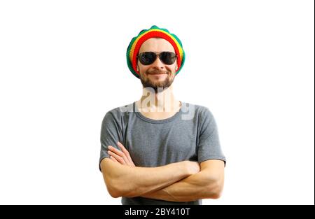 Young caucasian smiling man in rasta hat, sunglasses and grey t-shirt on white background laughing and having fun. Stock Photo