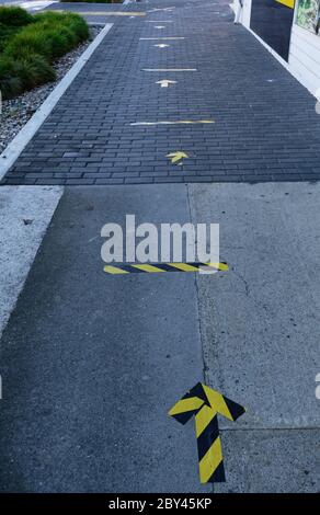 Yellow and black tape on the pavement to show where to stand to maintain safe distances from the person in front of you in the queue to enter a busine Stock Photo