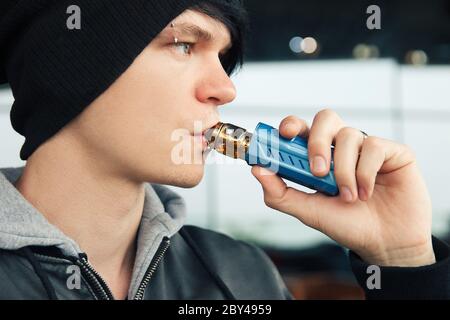 Young man in beany hat and hooded leather jacket smoking a vape Stock Photo