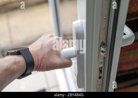 Homeowner seen gripping the handle of a newly installed uPVC high security door. Showing the multiple latch system and thick door frame. Stock Photo